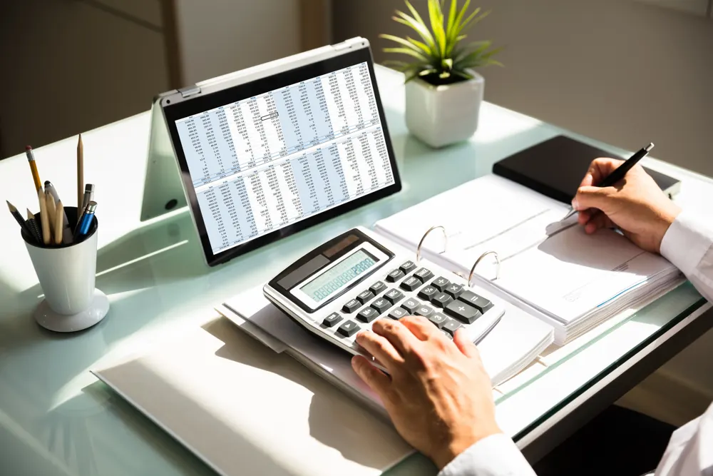 Hands working through invoices with a calculator and tablet